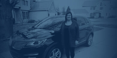 Woman standing next to her car in the driveway.